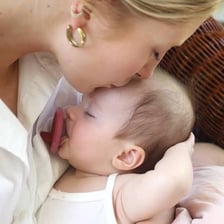 A baby using a pacifier while a mother sits nearby