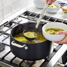 A cooking pot filled with soup on a stovetop.