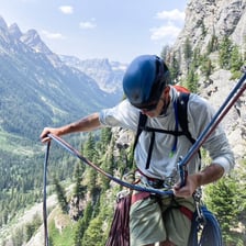 A rock climber secured by a rope on a cliff.