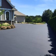 A residential driveway covered with dark asphalt pavement.