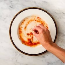 A piece of bread absorbing sauce from a plate.