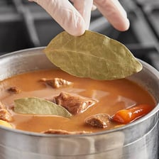 A bay leaf used as seasoning in a bowl of soup.