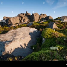 A steep, rugged rocky outcrop rising from a landscape.