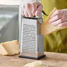 A hand shredding cheese with a box grater
