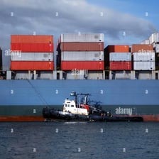 Tugboats maneuvering near a large ship in a harbor.