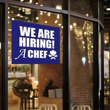Store window displaying a “We're hiring!” sign