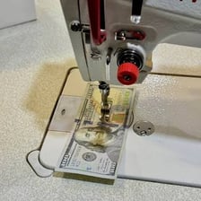 A sewing needle and thread beside a salary paycheque, representing the wordplay and definition.