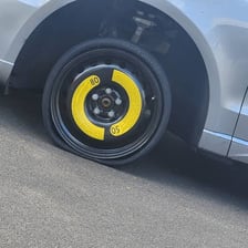 A spare tyre stored in a car beside a deflated road tyre