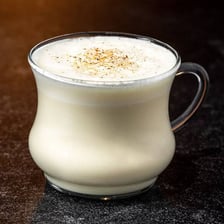 A glass of gin beside a mug of eggnog