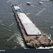 A broad, flat-bottomed barge travelling on a river.