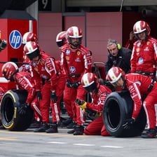 A racing car undergoing a pit stop by a team of mechanics.