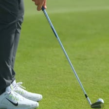 A golfer hitting a short chip shot toward the putting green