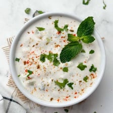 A bowl of cucumber raita garnished with herbs