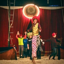 A clown performing in a circus ring under a big top