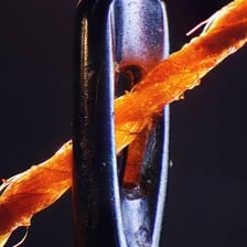 A metal sewing needle threaded with thread.