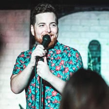 A comedian speaking to an audience on stage.