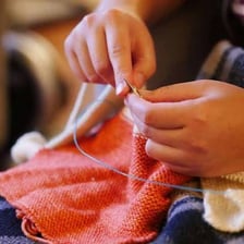 Hands using knitting needles to work wool yarn