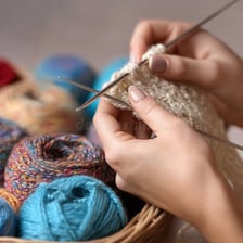 Hands using knitting needles to make a wool scarf