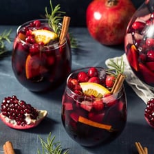 A glass of red sangria containing pieces of fruit.