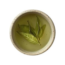 A cup of green tea beside loose green tea leaves.