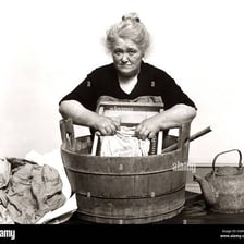 A woman washing clothes by hand in a historical laundry setting.
