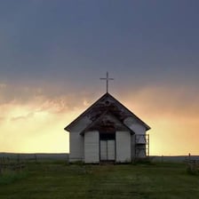 A clergyman standing outside a rural church.