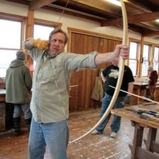 A craftsperson making a wooden bow in a workshop.