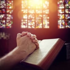 Clasped hands in prayer inside a church.