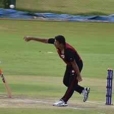 A cricket bowler delivering a ball on the pitch