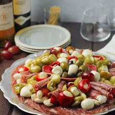 An Italian antipasti platter served beside a glass of wine.