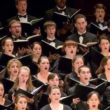 A choir singing together from the same musical score.