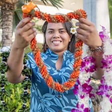 A person giving a Hawaiian greeting while wearing a flower lei.