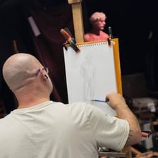 An artist sketching a model holding a pose in a studio.