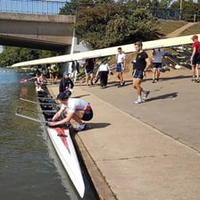 A rowing crew using oars to propel a boat on a river.