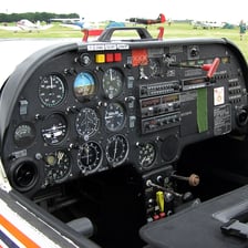 A pilot seated at the controls inside an aircraft cockpit.