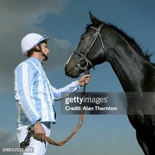 A jockey holding the reins while riding a racehorse.