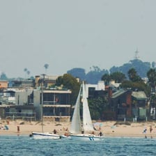 A sailboat positioned on the sheltered side of a landform.
