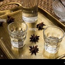 Anise seeds beside a glass of ouzo.