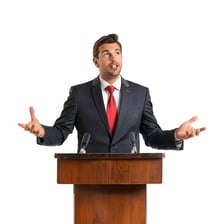 A speaker delivering a speech at a podium.