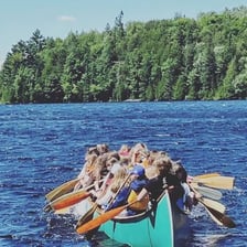 A canoe being paddled on a lake near a summer camp.