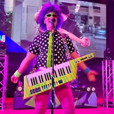 A musician plays a keyboard instrument worn on a shoulder strap.