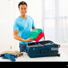 A traveler packing clothes into a suitcase