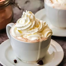 A warm mug of cocoa topped with whipped cream.