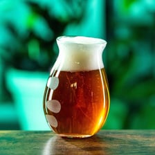 A pint of hazy IPA beer beside hop cones