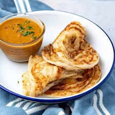 A flaky roti canai flatbread on a plate