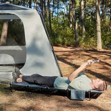 A folding cot set up inside a camping tent.