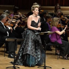 An opera singer performing with an orchestra onstage.