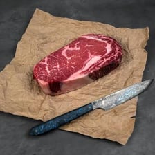 A raw boneless rib eye steak on a cutting board.