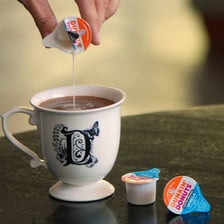 Small containers of coffee creamer beside a cup of coffee