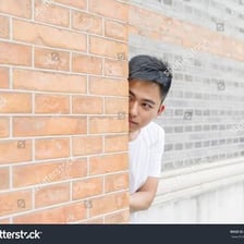 A person partially concealed behind a wall.
